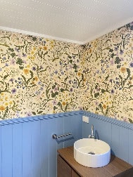 Small bathroom with floral wallpaper, blue wainscoting, a white round sink on a wooden vanity