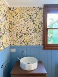 Bathroom with floral wallpaper and a blue wainscot panel. The sink has a round white basin