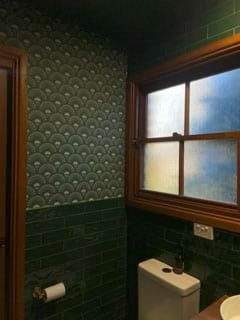 Bathroom with green fish scale pattern wallpaper, green tile wainscoting, and a frosted window