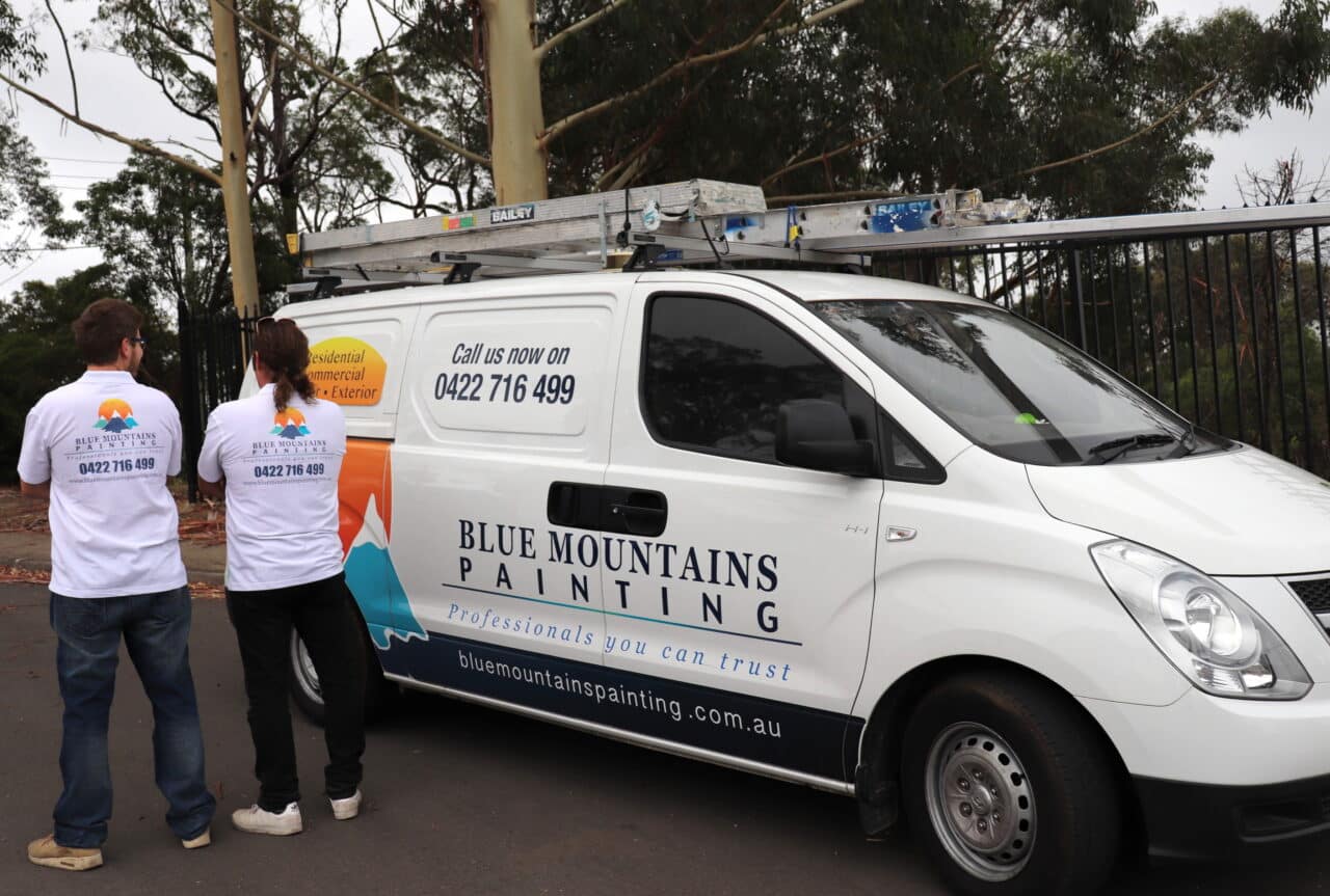 Two people in branded shirts are standing next to a Blue Mountains Painting van