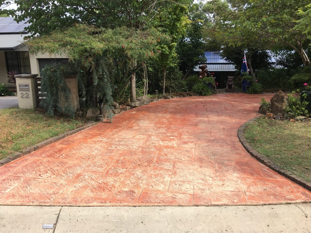A curved stamped concrete driveway with a terra cotta color leading to a house