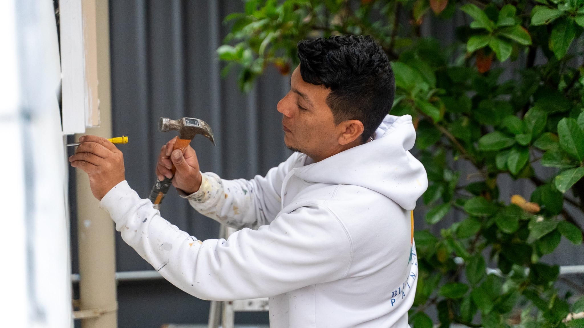 A person in a white hoodie using a hammer and a yellow measuring tool