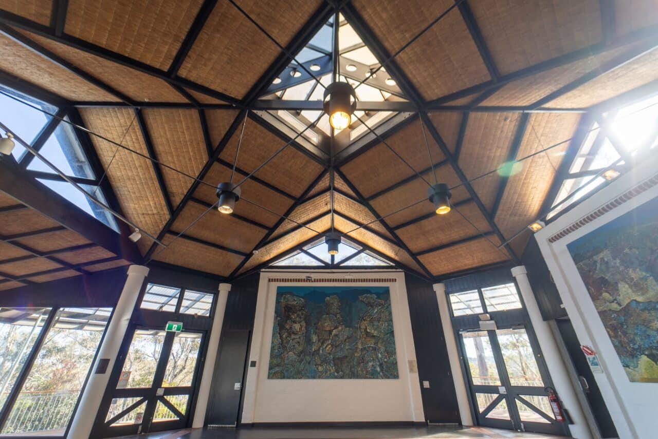 A spacious room with a high, triangular wooden ceiling reminiscent of a hut and large windows