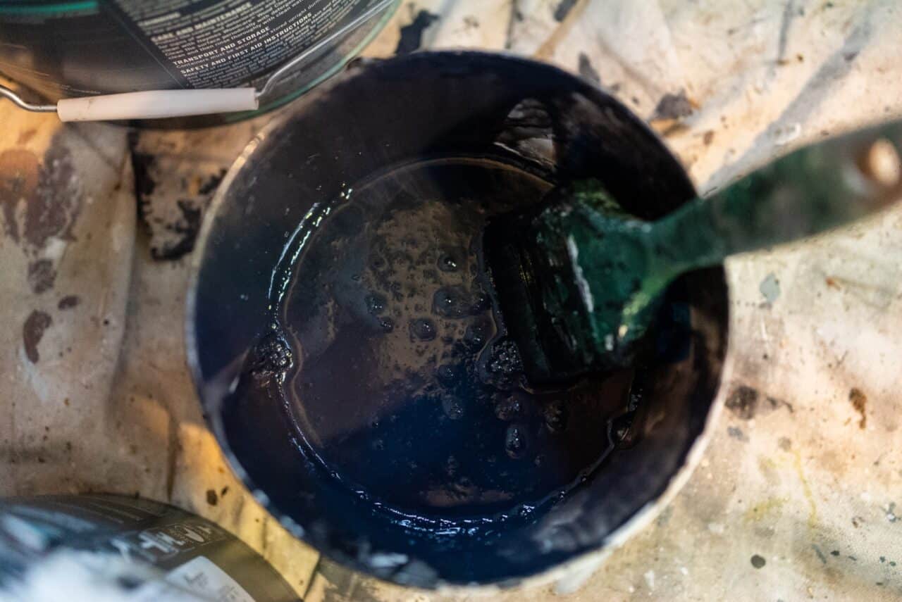 A paintbrush resting inside a container filled with dark blue paint.