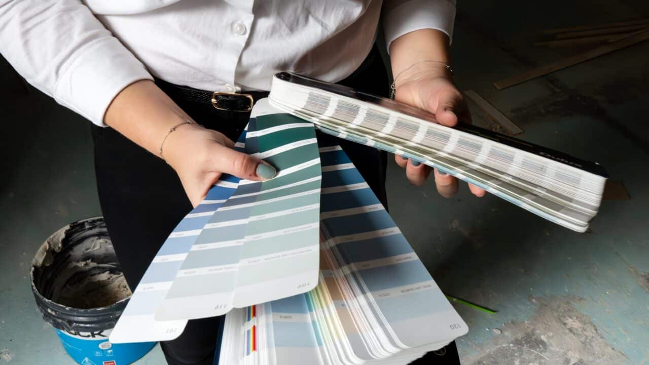 Person holding several color sample swatches, likely for paint, inside a room under renovation
